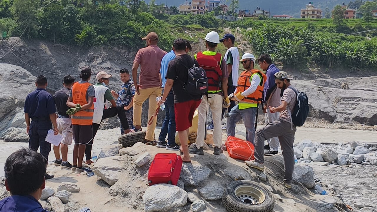 People and rescue workers gathered with luggage on the rocks beside the river