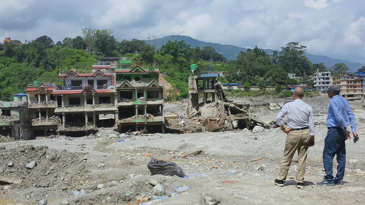 Two men looking out over collapsed buildings and a silt-filled riverbed